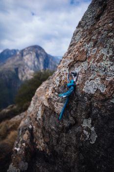 Close-up of a climbing anchor embedded in a rocky mountainside under a cloudy sky, showcasing outdoor adventure.