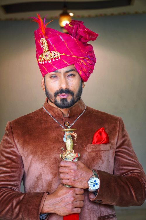 Free Portrait of a man with beard, in traditional attire and vibrant turban, holding a ceremonial sword. Stock Photo