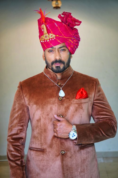 Free Confident man in traditional Indian attire and brass turban, standing indoors. Stock Photo