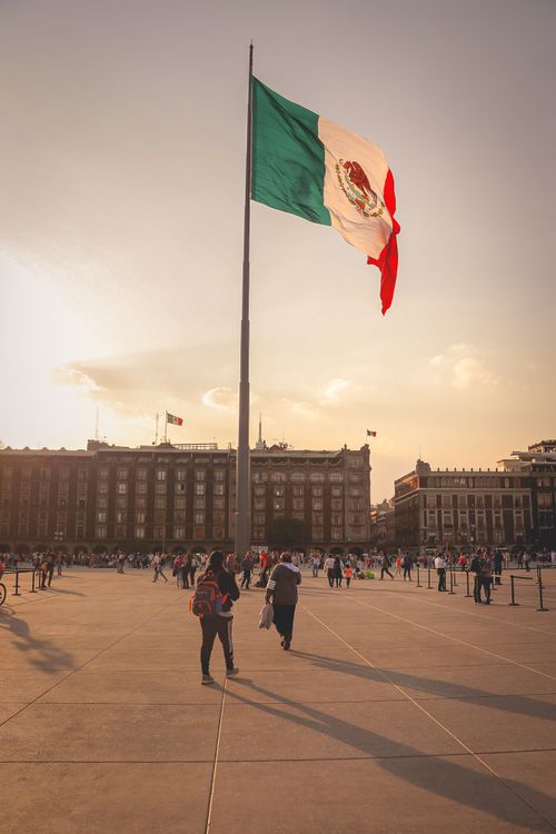 Free View of the Mexican flag waving over Zócalo Square in Mexico City during sunset, showcasing patriotism. Stock Photo