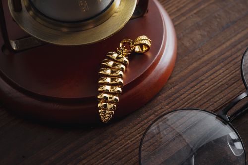 Free A close-up of a golden rattlesnake pendant on a wooden surface, beside a lamp and glasses. Stock Photo