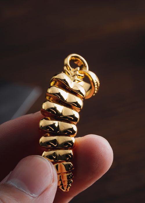Free Handcrafted golden dragon scale pendant with intricate detailing, held between fingers, ideal for jewelry enthusiasts. Stock Photo