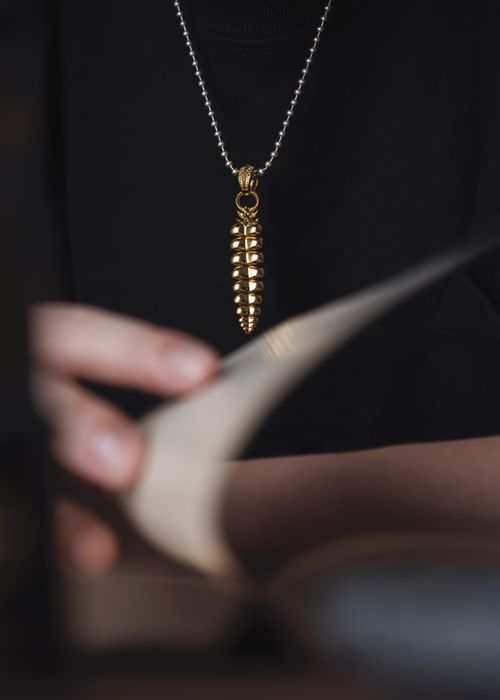 Free Close-up of a stylish gold pendant necklace, featuring a unique rattlesnake tail design, worn over a black t-shirt. Stock Photo