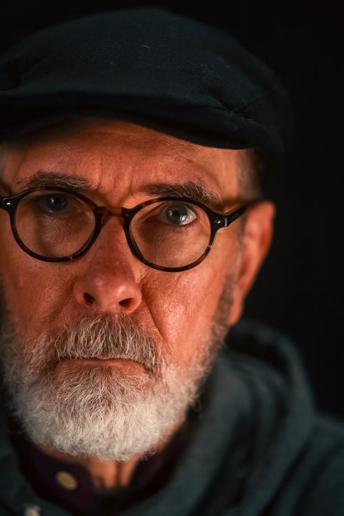 Free Close-up portrait of an elderly man with glasses wearing a cap, set against a dark background. Stock Photo