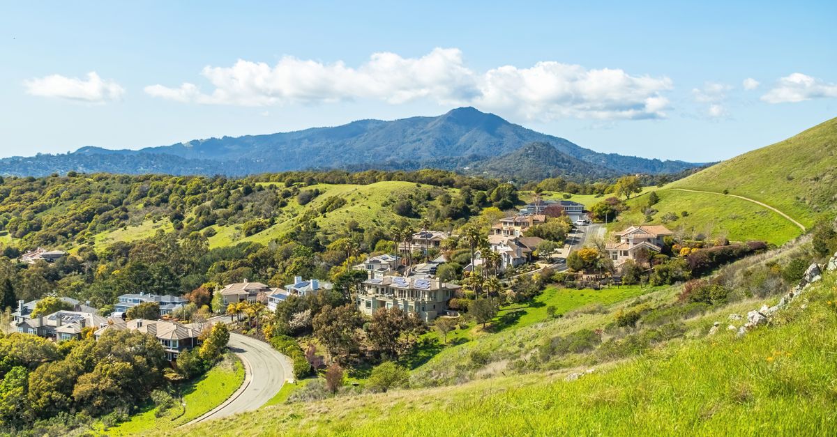 A picturesque town nestled in green hills with a mountain backdrop under a clear sky.