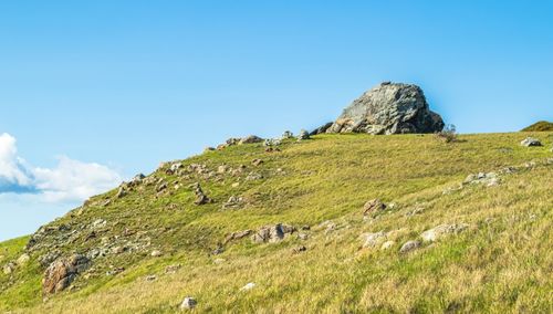 Free A breathtaking view of a grassy rocky hill under a bright blue summer sky. Stock Photo