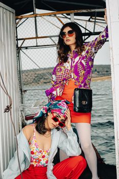 Trendy women posing in vibrant outfits by the water, showcasing summer style.