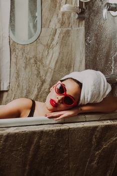 Fashionable woman with sunglasses and towel in a luxurious bathroom setting.