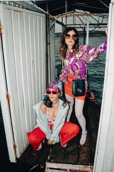 Stylish women posing in vibrant summer outfits near the seaside, showcasing modern fashion trends.