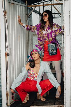 Two stylish women posing fashionably in bold, colorful outfits embodying modern fashion trends.