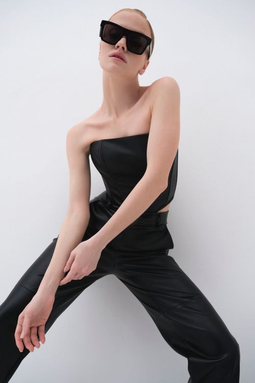 Free Chic woman posing in black attire with sunglasses on a white background. Stock Photo