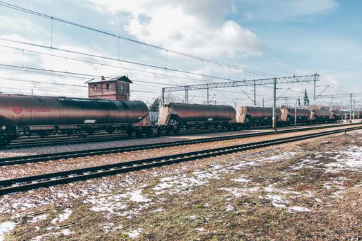 A cargo train transporting goods on railway tracks in a snowy outdoor setting under a cloudy sky.