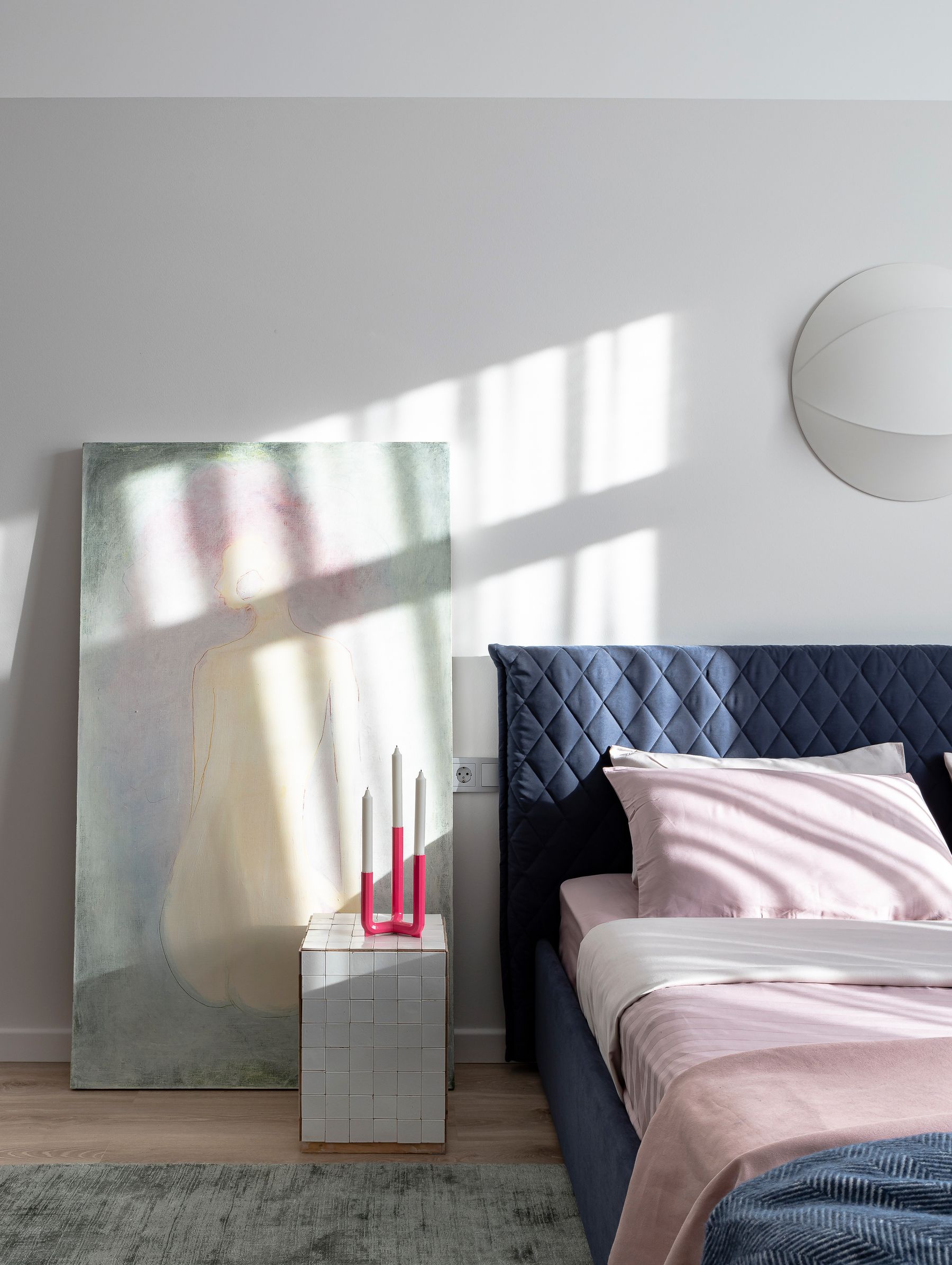 Modern bed with a blue bedspread and blue pillows crossed by warm directional sunlight