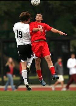Two soccer players in mid-air challenge on a green field during a game.