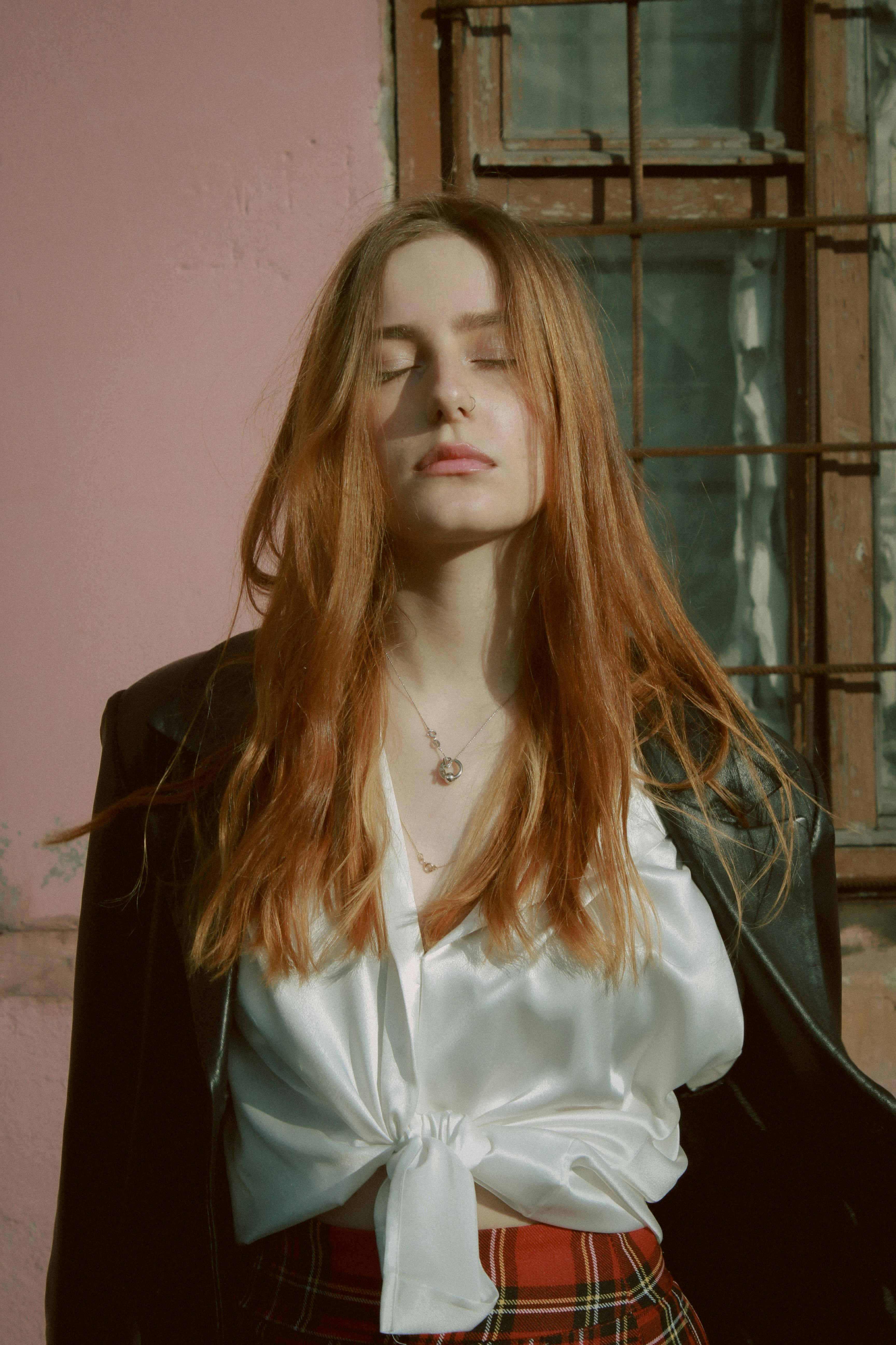 A redhead woman in a blouse and jacket posing outdoors.