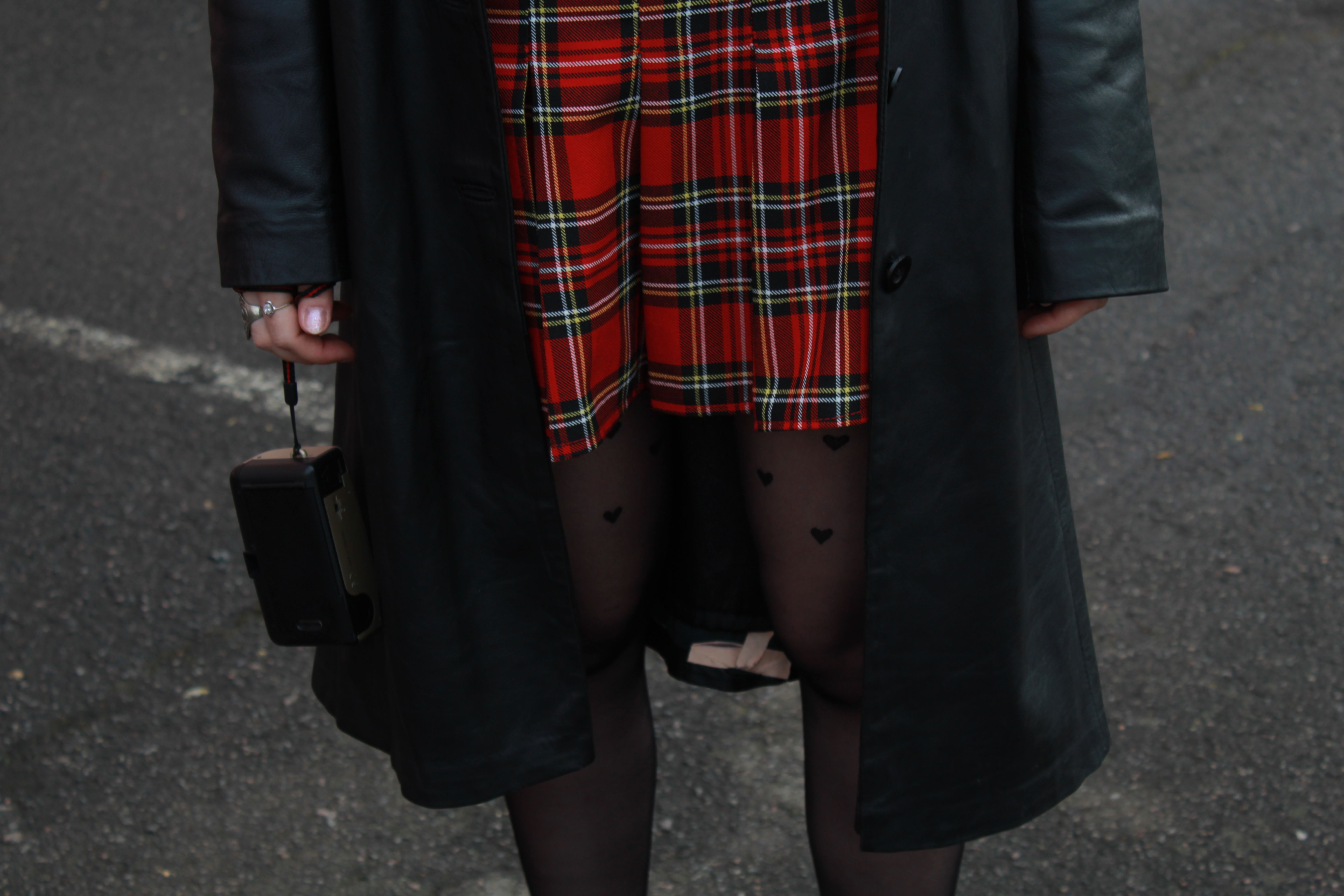 Close-up of a woman in a plaid skirt and leather jacket holding a vintage camera.