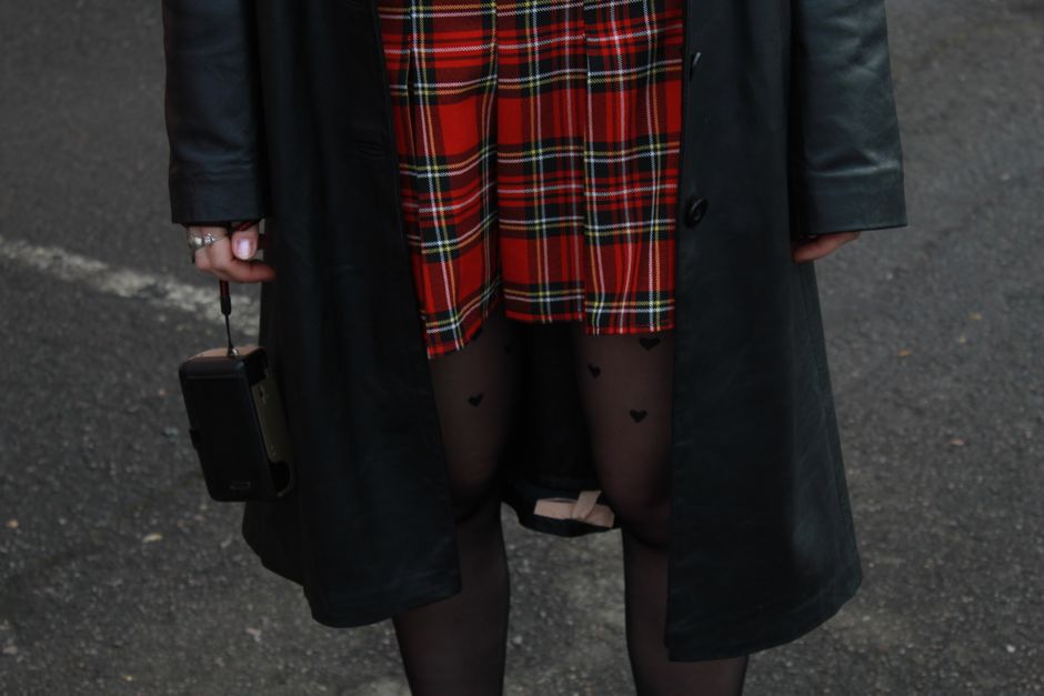 Close-up of a woman in a plaid skirt and leather jacket holding a vintage camera.