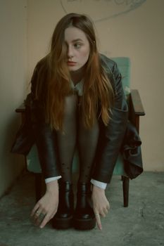 A young woman with long brown hair sitting on an armchair, stylishly dressed in black indoors.