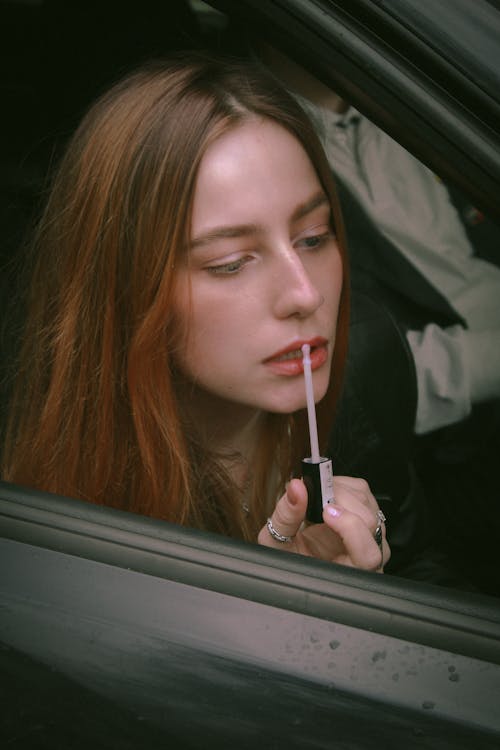 Woman in a Car Looking at her Reflection in a Side Mirror and Applying Lipstick 
