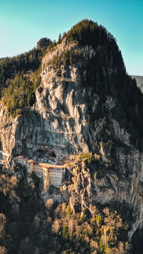 Free A stunning aerial view of a monastery built into towering rocky cliffs, surrounded by dense forest. Stock Photo