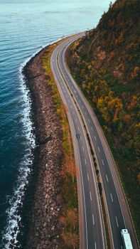 A stunning aerial shot of a winding coastal road along the sea with adjacent forested hills.
