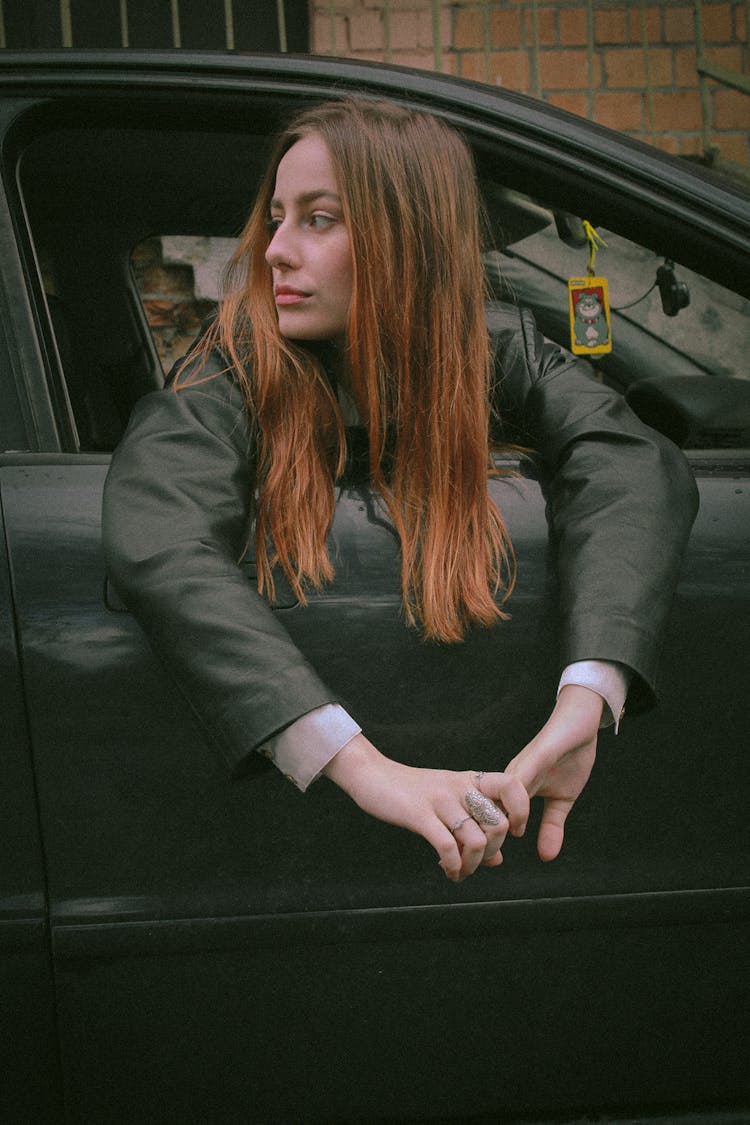 Young Woman Sitting In A Black Car And Looking Out The Window 