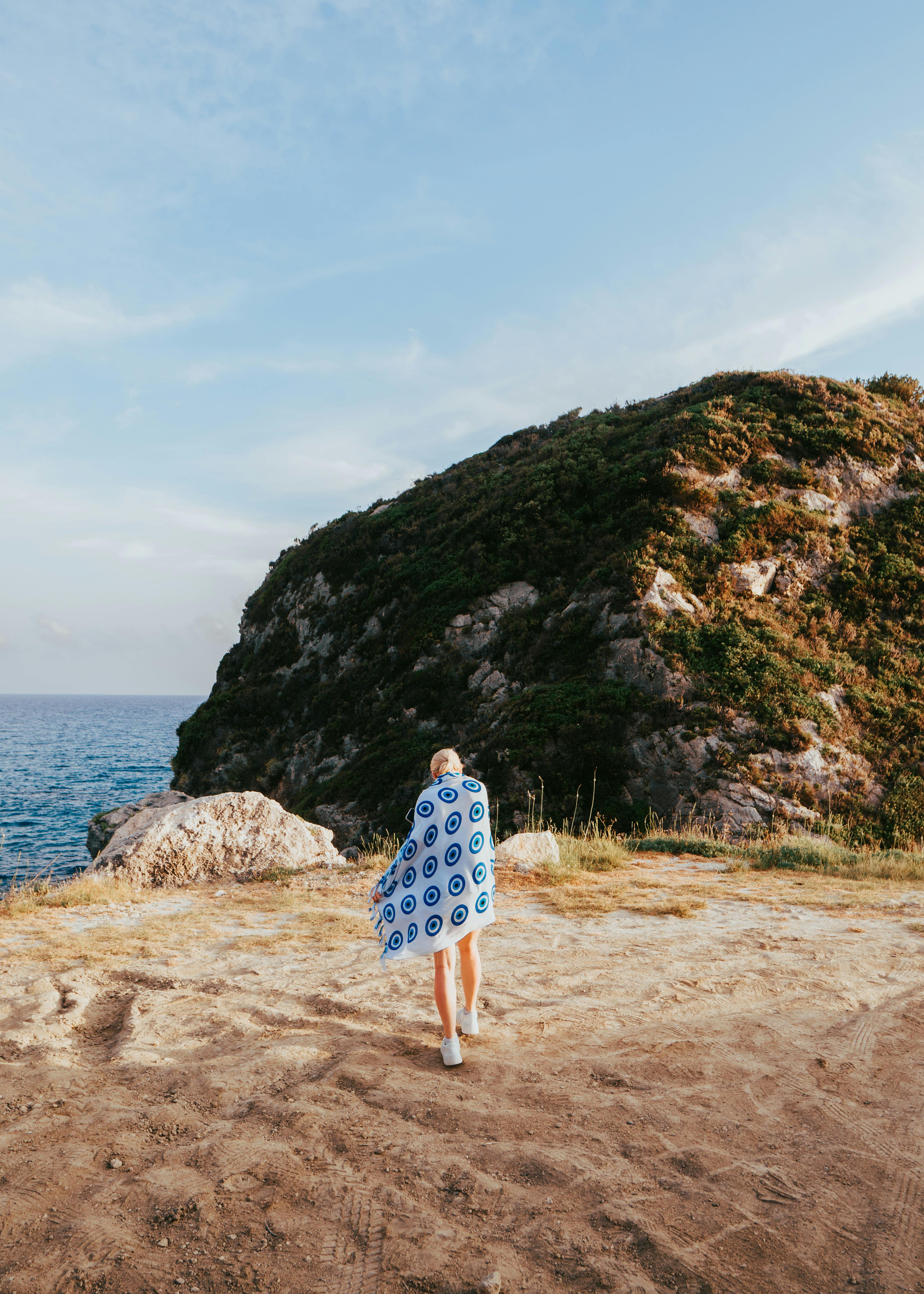 A person wrapped in a towel stands on a cliff overlooking the sea, capturing a serene coastal landscape.