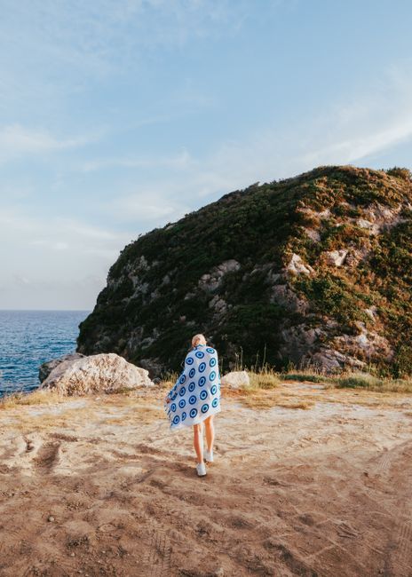 A person wrapped in a towel stands on a cliff overlooking the sea, capturing a serene coastal landscape.