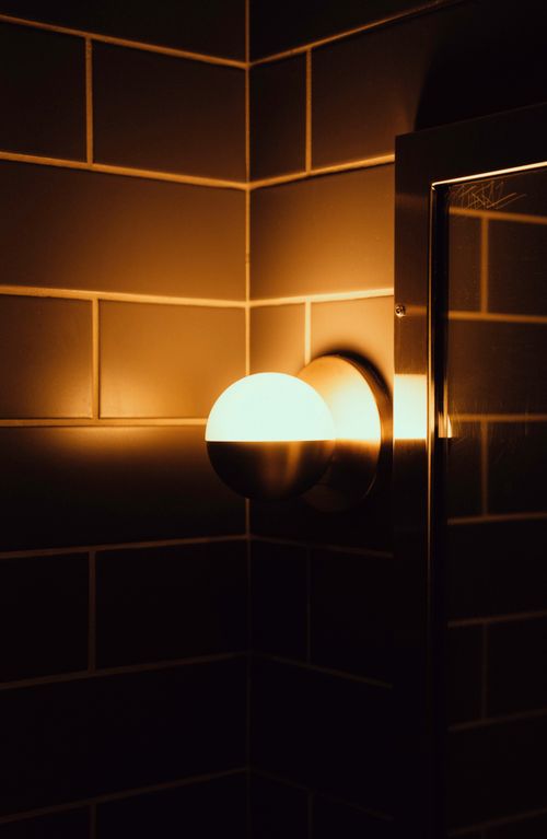 Free Elegant bathroom interior with a modern lamp and tiled walls, creating a warm ambiance. Stock Photo