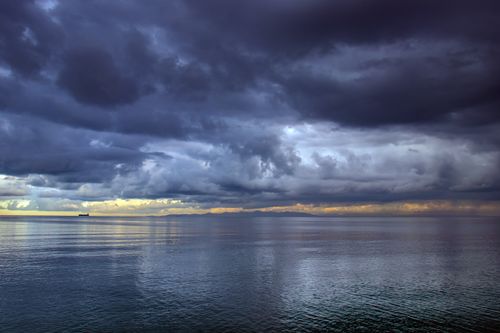 Free A ship sails under dark, dramatic clouds on a calm sea near Radès, Tunis at sunset. Stock Photo