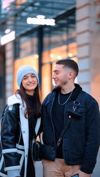 A happy couple smiling and standing together in a modern urban environment during winter.
