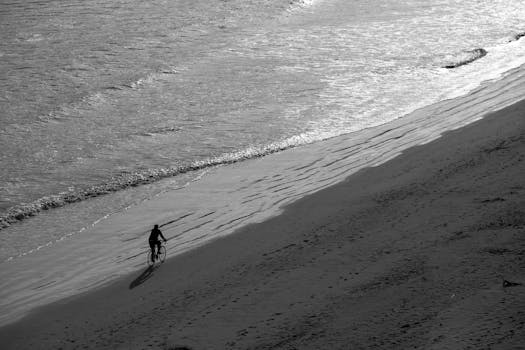Black and white photo of a cyclist riding on the sandy shores of Pismo Beach, CA.