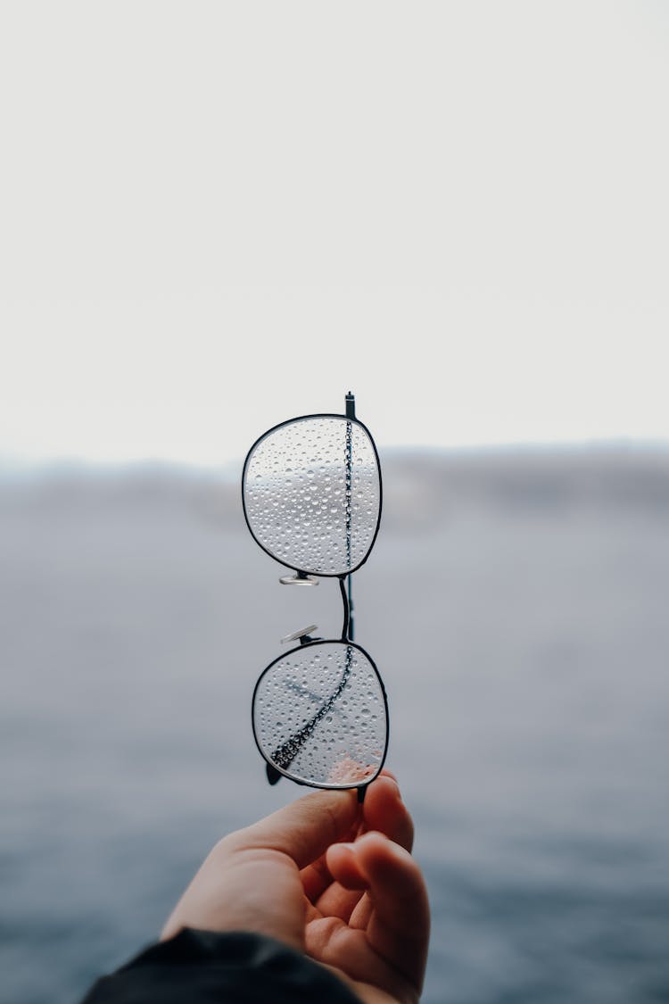 Close-up Of A Man Holding Wet Eyeglasses In His Hand 