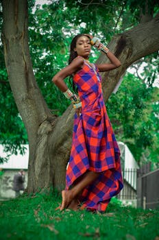 Beautiful fashion portrait of a woman in a checkered dress posing gracefully by a tree