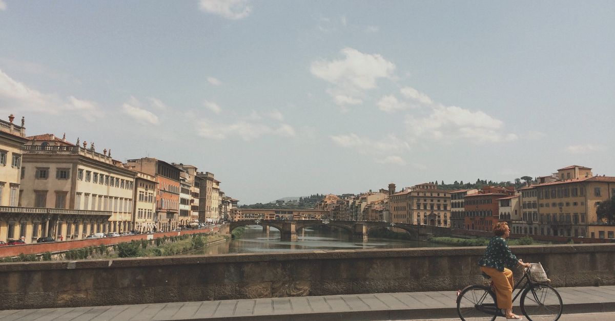 Woman cycling beside the Arno River with historic Florence in the background.