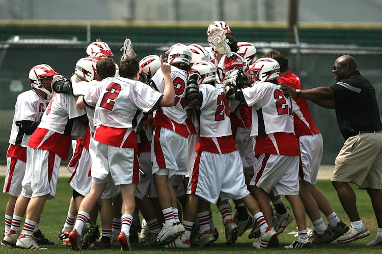 Group Of Lacrosse Players Celebrating With Coach During Daytime