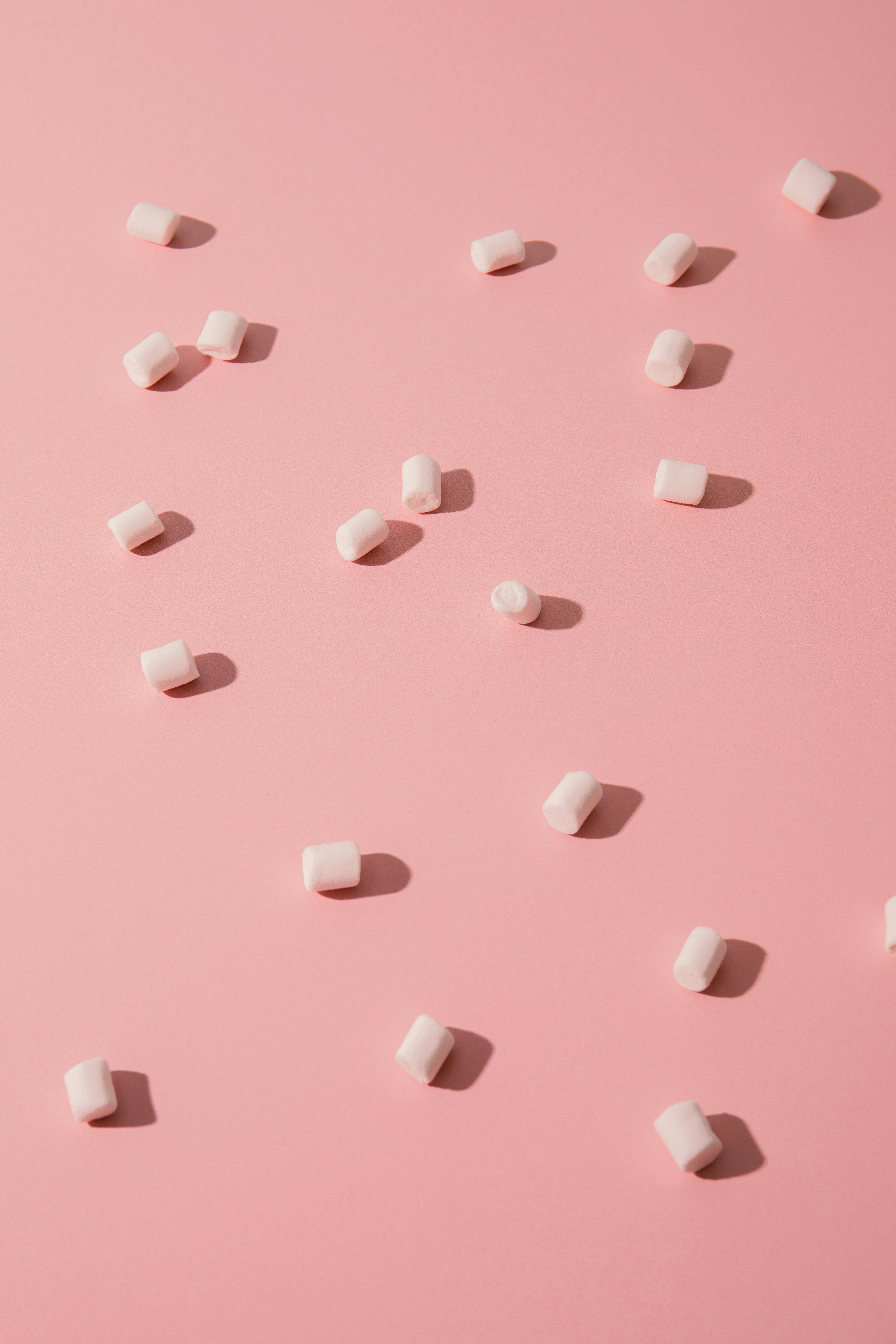 Top view of white marshmallows scattered on a pastel pink surface for a sweet, soft aesthetic.