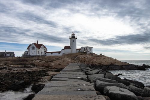 Free A lighthouse on a rocky shoreline under overcast skies, ideal for nautical themes. Stock Photo