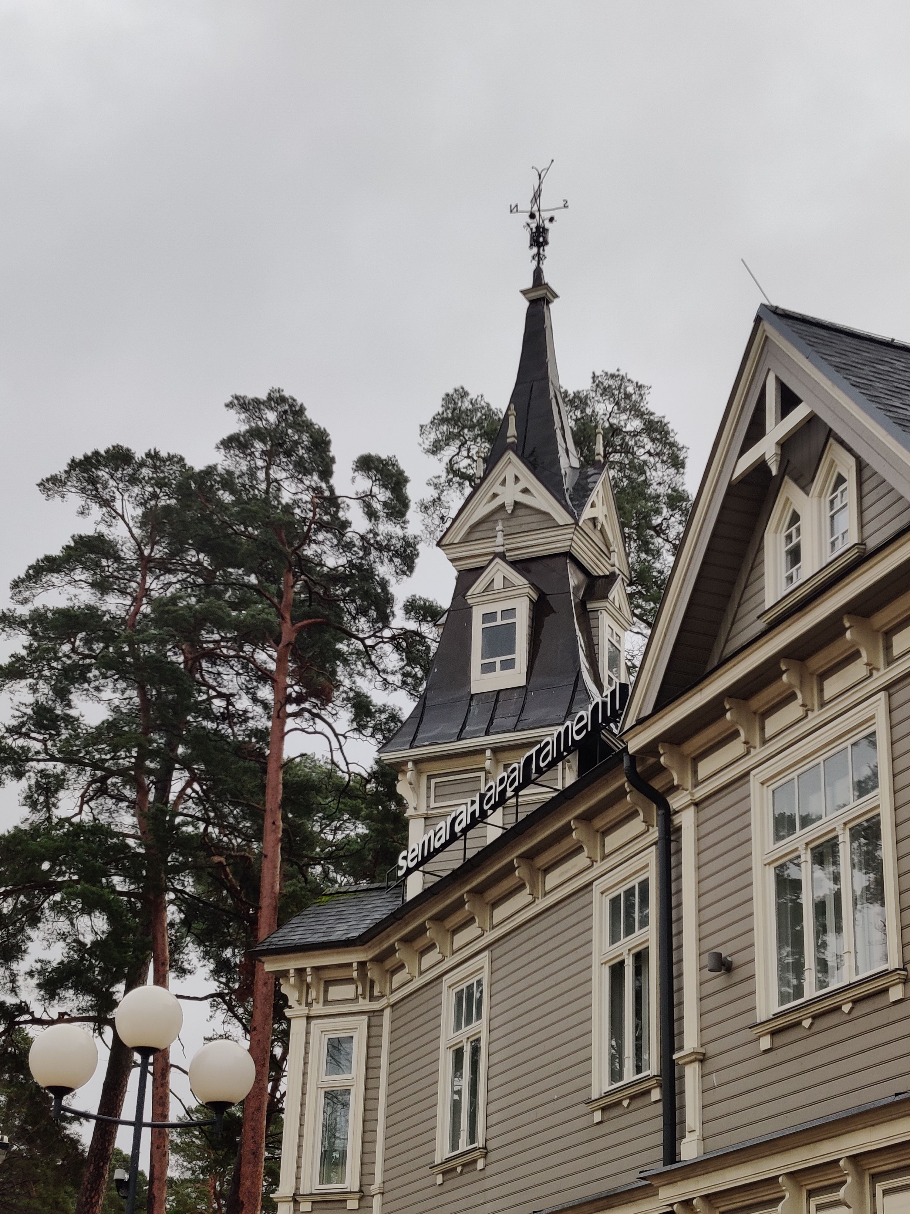Charming historic wooden building featuring a tall steeple and surrounded by lush trees on an overcast day.