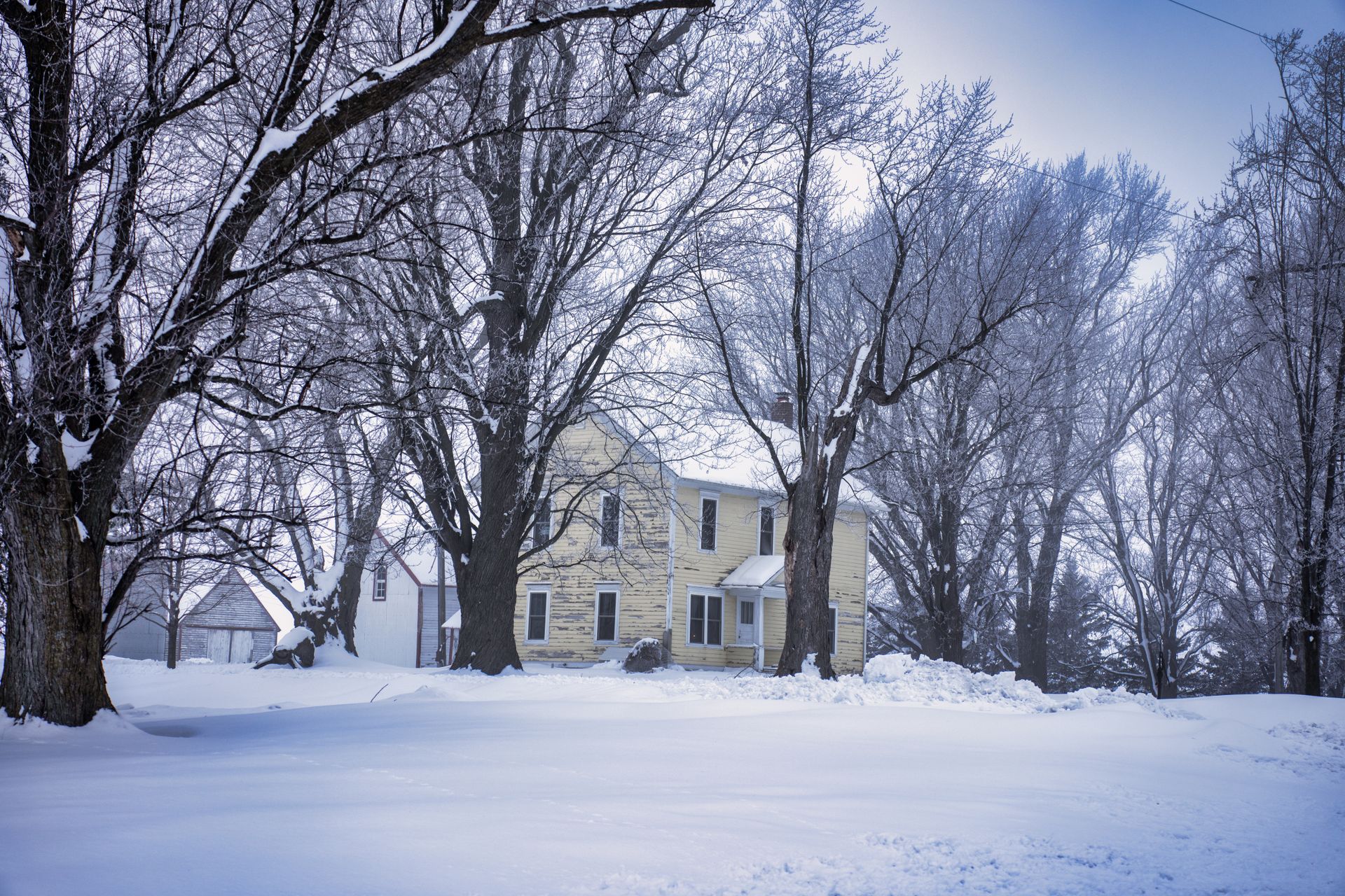 A peaceful rural house in snowy Minnesota surrounded by bare trees during winter.