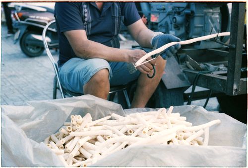 Free A man sitting outside cutting plastic tubes, showcasing industrial work in progress. Stock Photo