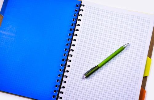 бесплатная Зеленая и серебряная ручка на белой бумаге в линейку в помещении Стоковое фото