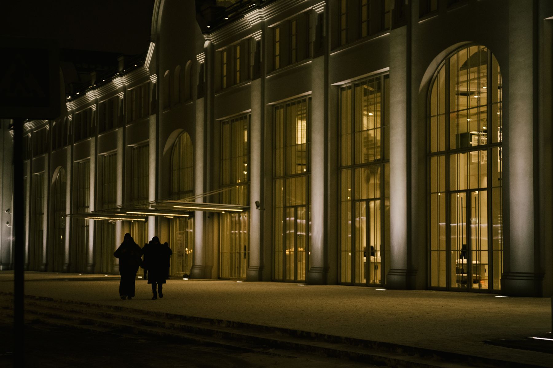 Illuminated glazed commercial frontage in the evening, the glass reading as the architecture of the building