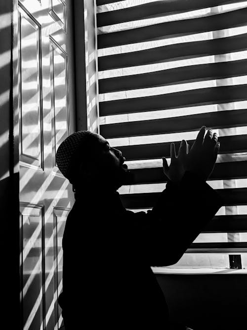 Man Praying in Front of a Blinded Window