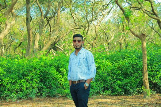 Man in casual attire posing confidently in a vibrant green forest during summer.