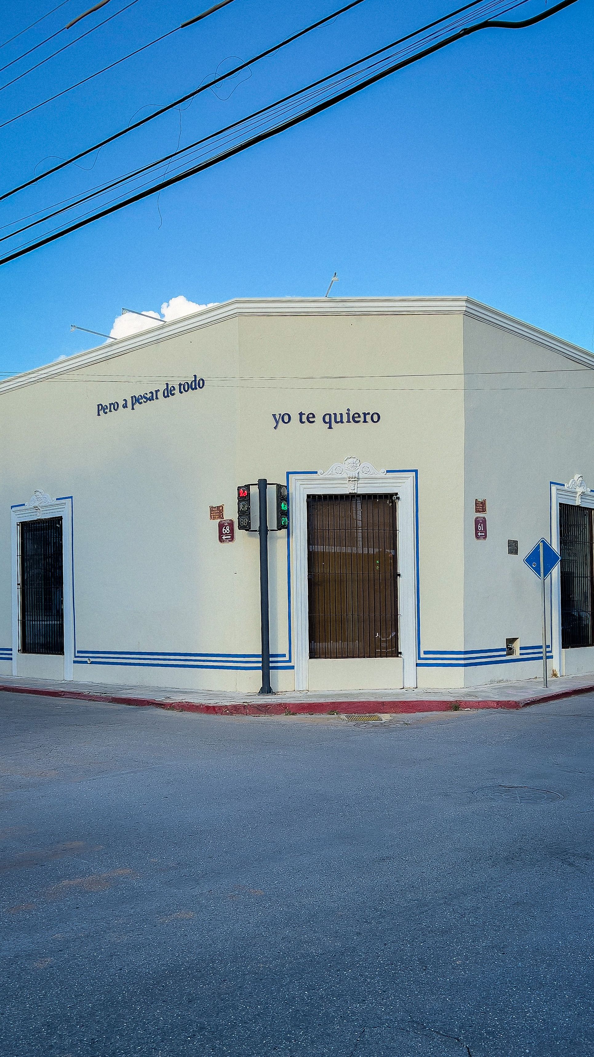 Urban street corner with romantic Spanish love quotes on building facade, blue sky, and clear street view.