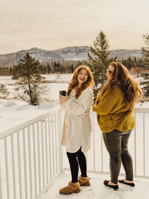Two Young Women Standing on a Snow-Covered Balcony with Hills in the Background
