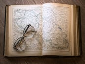 一张木桌上摊开着一本书，书上放着一副眼镜，旁边是一张老式地图的特写
