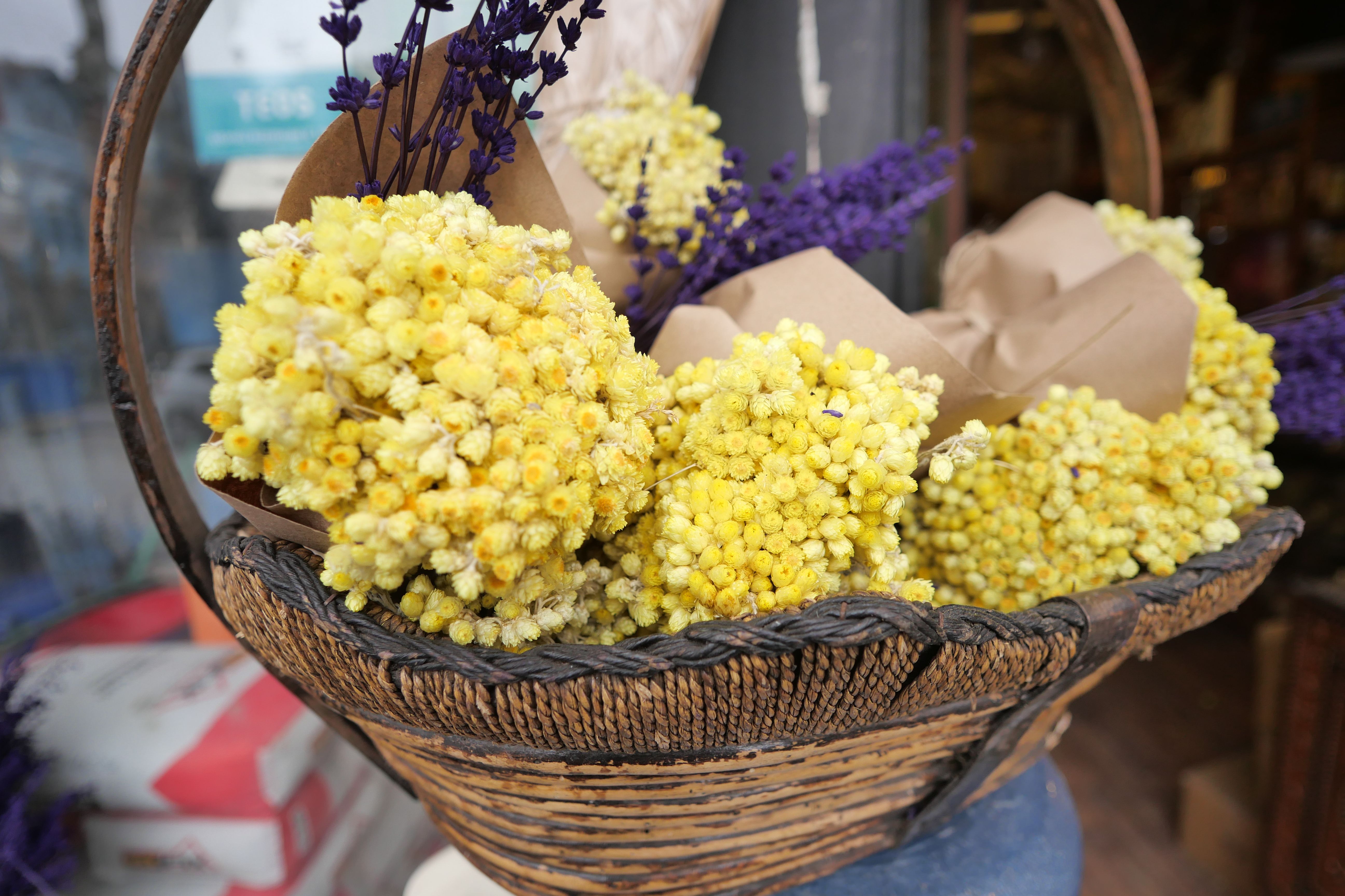 A charming mix of dried yellow and purple flowers in a rustic wicker basket, perfect for decor.