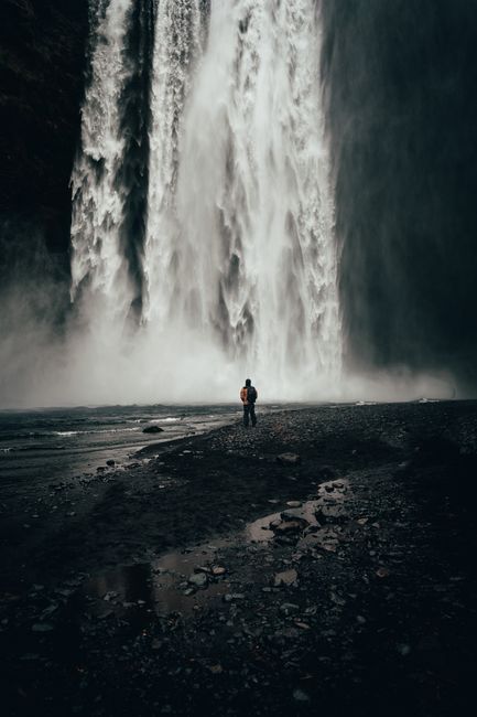 A person stands in awe at the base of Skógafoss, a stunning Icelandic waterfall.
